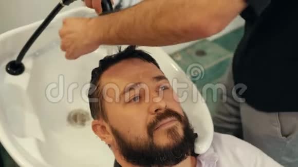 男理发店洗头时留着胡子的人画像在男性沙龙里面对成年男子洗头头发视频的预览图