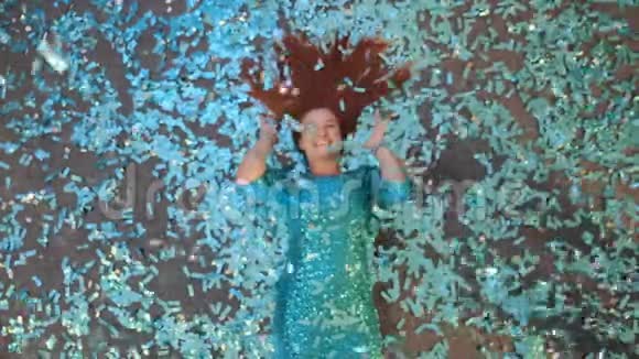 红发美女躺在蓝色纸屑的地板上视频的预览图