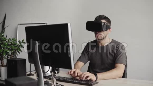 年轻人戴着虚拟现实护目镜耳机坐在办公室里对着电脑打字视频的预览图