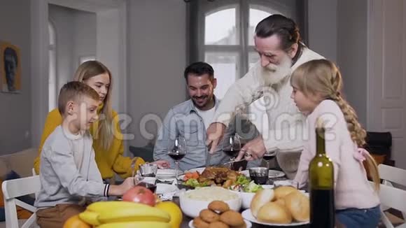 呼吁60岁的胡子爷爷雕刻美味的烤火鸡为他的家人聚集在餐桌旁视频的预览图