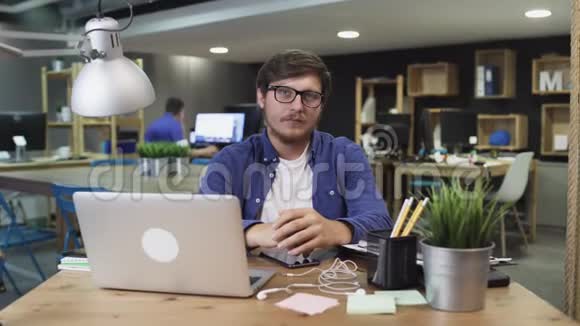 幸福企业主的肖像好看的胡须男戴着眼镜坐在创意办公室看着相机视频的预览图