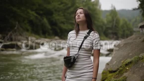 美丽的女人望着远处站在森林里的河岸上那个女孩在森林里徒步旅行连接视频的预览图