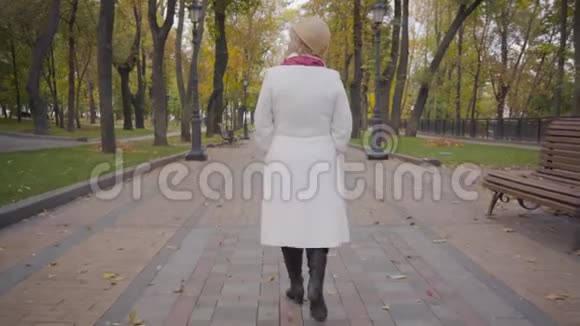 在小巷里漫步的白种人女人穿着优雅的米色紧身帽和白色外套成熟的女士休息视频的预览图