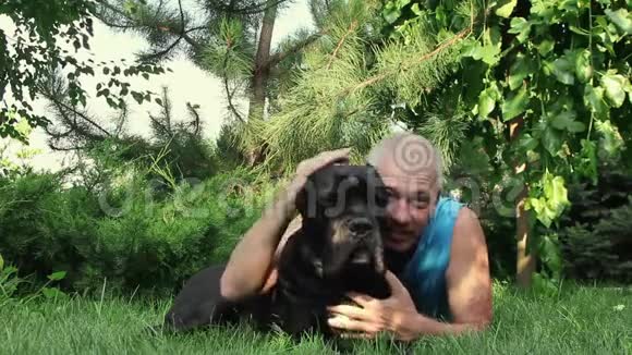 年轻人他心爱的黑藤萝狗躺在杉树下的绿草上视频的预览图
