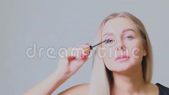 漂亮的金发女人在镜子前的睫毛上涂上睫毛膏美容和化妆概念视频的预览图