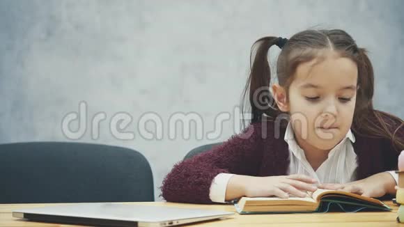 一个女学生坐在桌子旁在这段时间里他读了一本书合上书拿着笔记本电脑很开心在一个视频的预览图