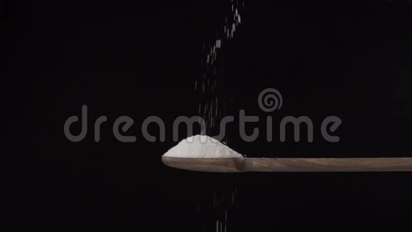 盐从上面倒入一个木勺隔离在黑色背景上视频的预览图