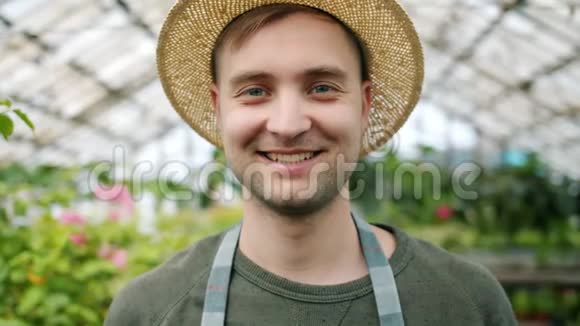 戴着帽子围裙戴着温室的英俊年轻园丁的特写肖像视频的预览图