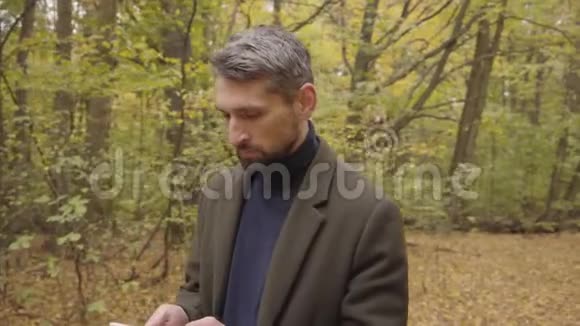 英俊的白种人站在秋天的森林里拿着石碑环顾四周自信的游客用他的小玩意视频的预览图