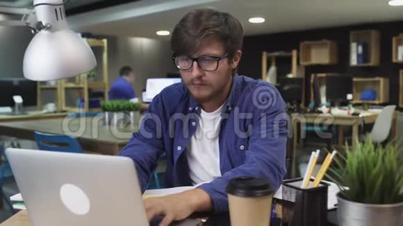 带眼镜的年轻人在办公室里用笔记本电脑工作视频的预览图