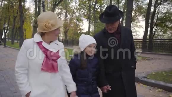 一对高加索族夫妇和一个戴着白帽子的女孩沿着小巷散步祖父母周末视频的预览图