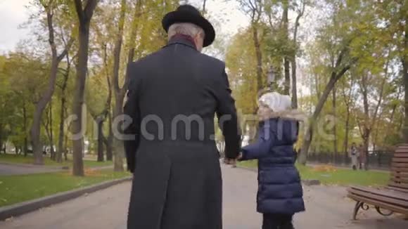 一位戴着优雅黑帽和外套的白种人成年男子与他的孙女漫步在小巷的背面视频的预览图