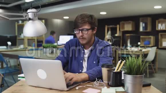 商务人士坐在他的办公桌前在时尚办公室的台式电脑上工作拿起智能手机开始工作视频的预览图