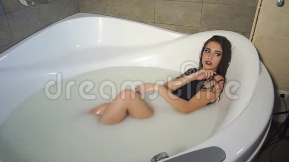 一个穿着黑色泳衣长发的性感女孩躺在满是牛奶的浴室里视频的预览图