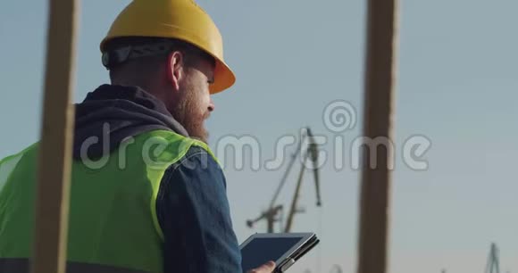 一个戴着黄盔胡子的码头工人在海岸的背景下使用平板电脑领班视频的预览图