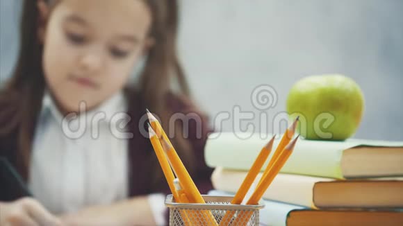 在灰色背景下关闭女学生在这段时间里他坐在桌子旁用铅笔拿起一本笔记本视频的预览图