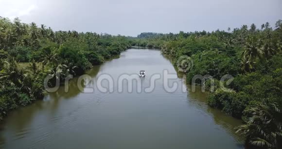 在丛林热带雨林荒野中一艘白色的小船在宁静的河流中远离相机航行视频的预览图