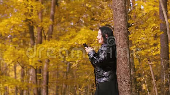 一位年轻的黑发女子站在一棵树旁正在打电话视频的预览图