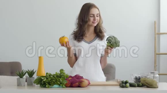 肖像年轻女子拿着黄色番茄和西兰花站在现代厨房的桌子上健康食品的概念视频的预览图