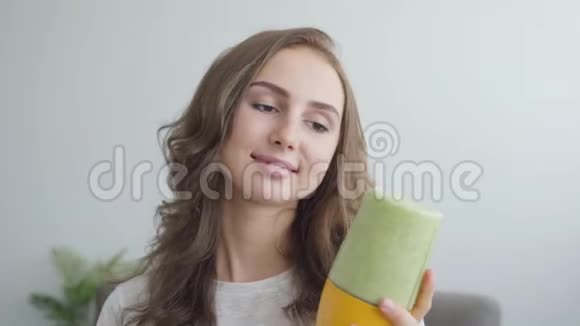 年轻微笑的女人在家里厨房的摇床上做奶昔的肖像健康食品的概念视频的预览图