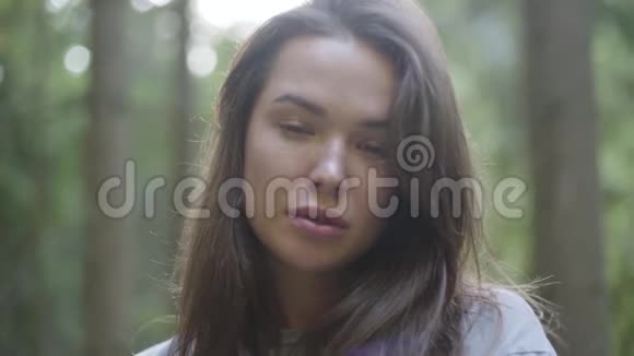 一幅可爱的女人在绿色森林里站在阳光下向外看的肖像那个女孩在森林里徒步旅行视频的预览图