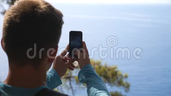 无法辨认的人在他的智能手机上拍摄风景迷人的海景年轻人用手机拍漂亮的照片视频的预览图