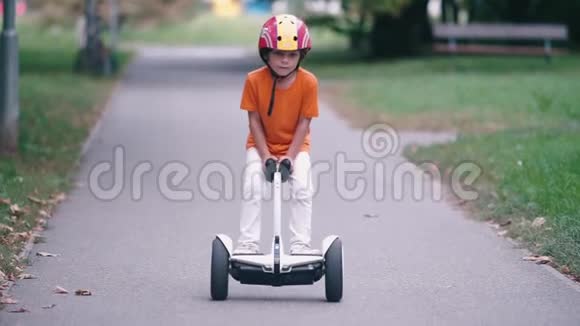 一个穿着橙色T恤的孩子沿着一个城市公园的小路骑着赛格威视频的预览图