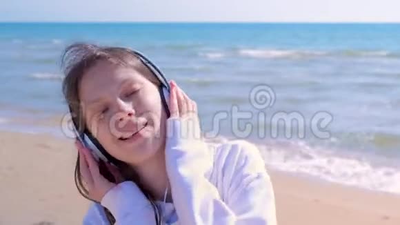 戴耳机的年轻女人的肖像喜欢在沙滩上散步视频的预览图