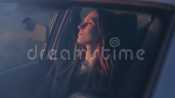 可爱的女性坐在车里休息在傍晚日落时闭上眼睛视频的预览图