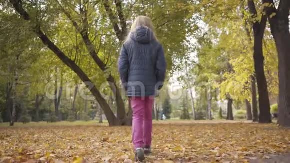 一个年轻的白种人少女在秋天公园散步穿着粉红色裤子和暖色蓝色夹克的少年视频的预览图