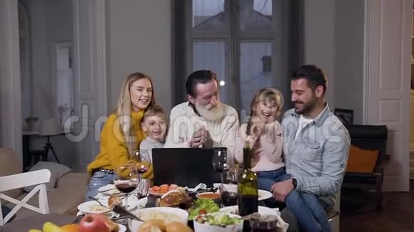 在节日餐桌上一家人在电脑上观看有趣的照片视频的预览图