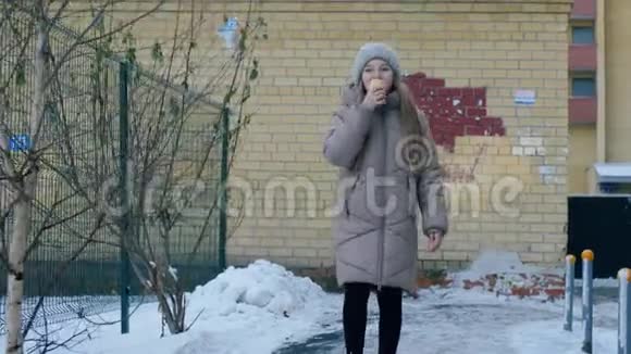穿着帽子和外套的年轻女孩在雪城冬天吃冰淇淋在冬城散步的快乐少女视频的预览图