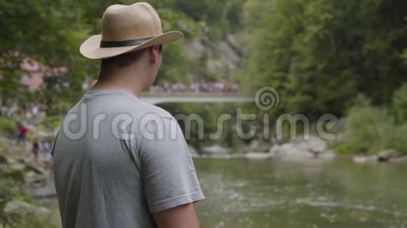 戴着帽子的帅哥在森林里看着河与自然的联系旅行度假视频的预览图