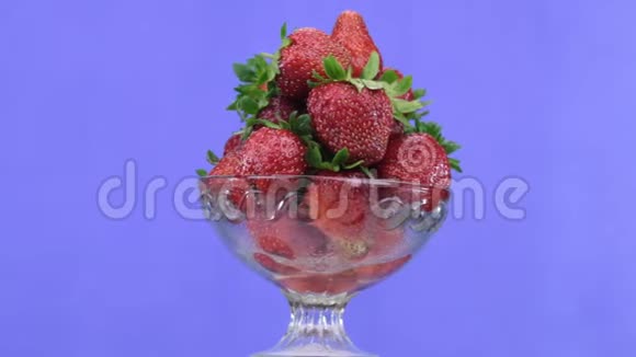旋转玻璃花瓶里的一堆草莓蓝色背景视频的预览图