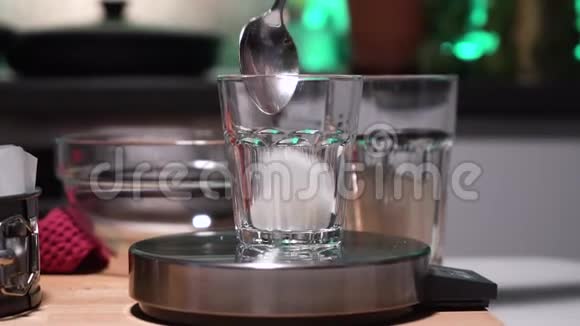 鳞片上的透明玻璃女孩或女人的手倒进玻璃里玻璃站在天平上糖在厨房里视频的预览图