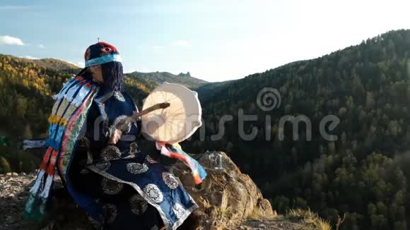 一个萨满敲着坐在山顶岩石上的手鼓视频的预览图