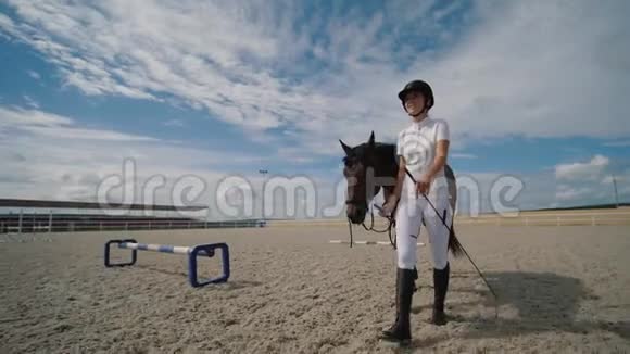 年轻女子骑马者与棕马牵着缰绳在沙骑竞技场散步视频的预览图