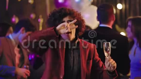 在大型派对上一个留着卷发拿着一杯香槟在镜头前的迷人而有趣的家伙正在享受视频的预览图