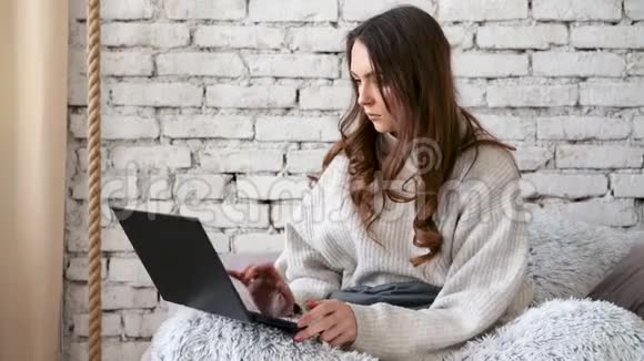 漂亮的女人坐在家里的床上用笔记本电脑工作视频的预览图