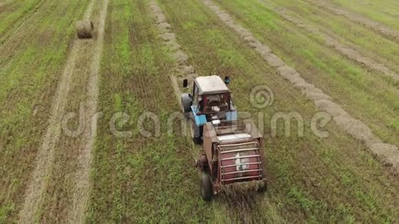 一种拖拉机有一个带牵引的打包机在收获的农田上用稻草打包视频的预览图