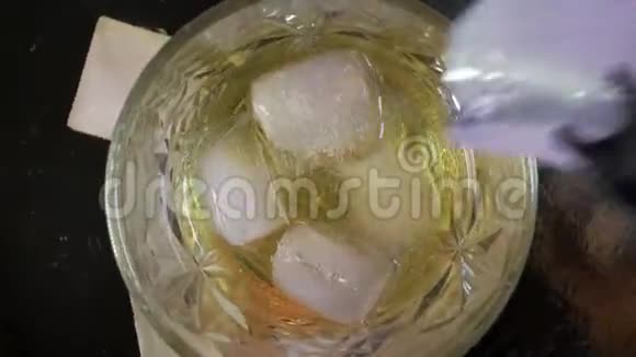 冰立方体的俯视图落下来融化在一杯威士忌中加冰的金色威士忌旋转一杯威士忌视频的预览图