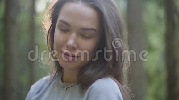 一幅可爱的女人在绿色森林里站在阳光下向外看的肖像那个女孩在森林里徒步旅行连接视频的预览图