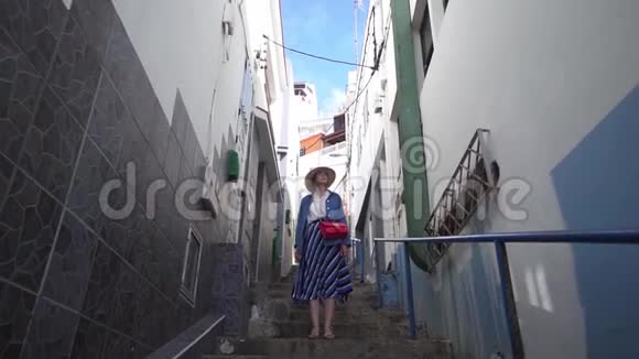 一个漂亮的女人站在西班牙房子之间的一条狭窄的街道上一个色彩斑斓的欧洲城市的街头游客视频的预览图