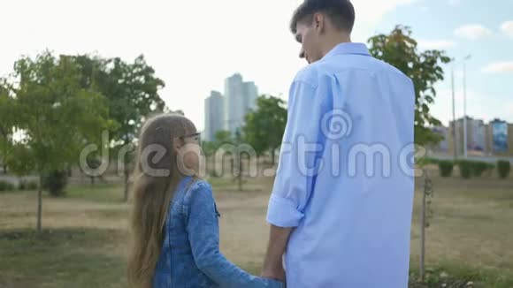 在城市的背景下哥哥牵着妹妹的手在公园里愉快地交谈视频的预览图