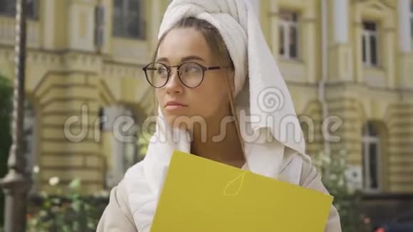 一幅可爱的年轻女人穿着浴袍头上戴着毛巾手里拿着文件夹站在街上这就是视频的预览图