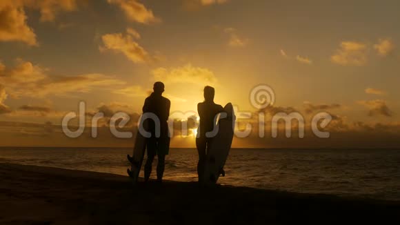 在热带海滩日落时手持长冲浪板的冲浪情侣视频的预览图