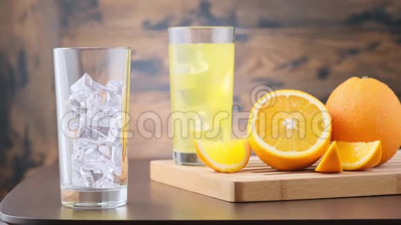 在装有冰块的玻璃杯中倒入橙汁汽水木制背景带有橙色水果视频的预览图