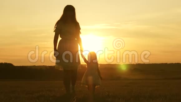 快乐童年的概念快乐的妈妈和宝宝在日落时分手牵着手笑着走在田野上小女孩视频的预览图