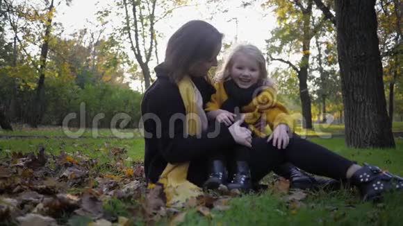 无忧无虑的童年年轻迷人的女妈妈和她迷人的微笑的女儿坐在草坪上走进来视频的预览图
