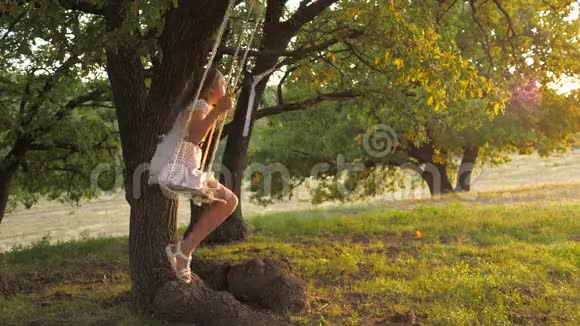 快乐的童年概念在日落公园的橡树枝上孩子们用绳子摆动女孩笑高兴少女视频的预览图